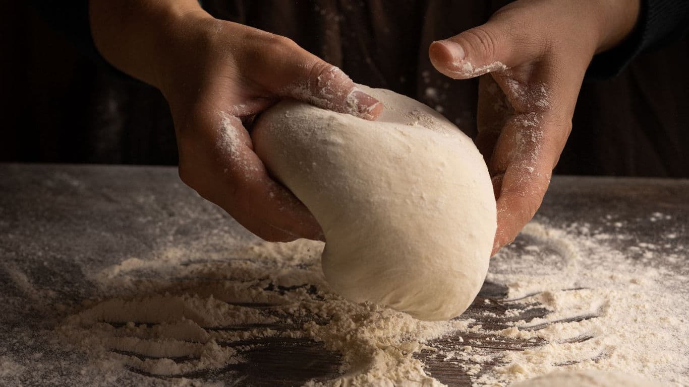 Hands Kneading Fresh Dough on Floured Surface