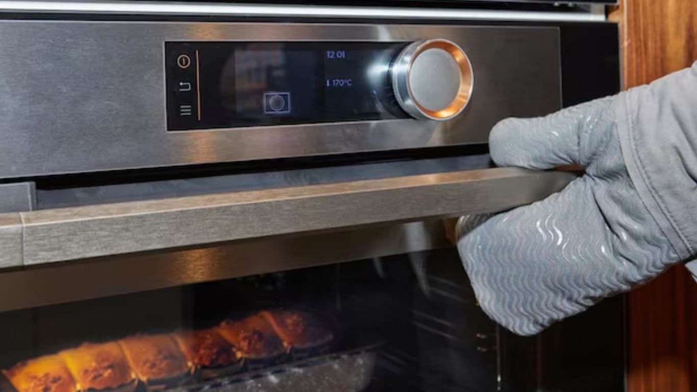 Person Opening Modern Oven With Oven Mitt