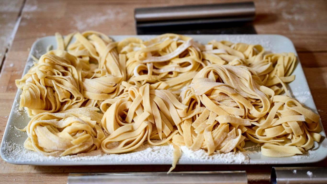 Fresh homemade fettuccine pasta on floured tray
