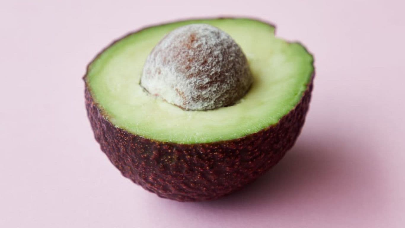 Fresh avocado half on pastel pink background