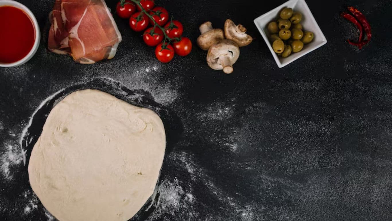 Pizza Dough with Fresh Ingredients on Black Surface