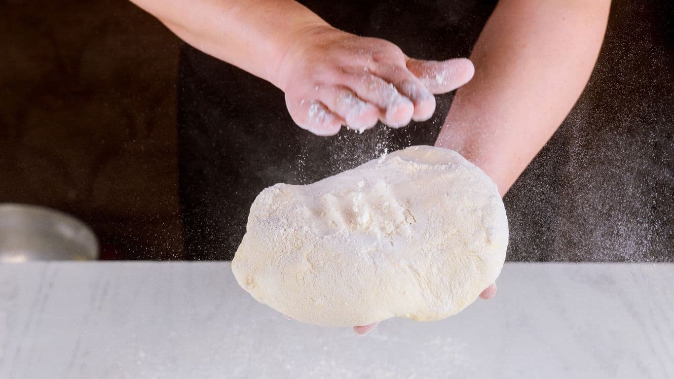 Person dusting flour on fresh bread dough