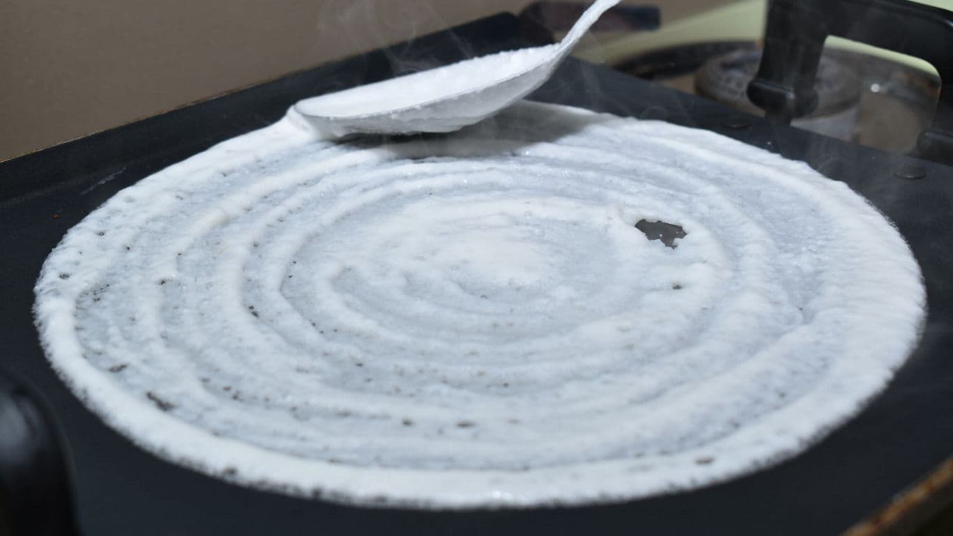 Spreading dosa batter on hot griddle with ladle