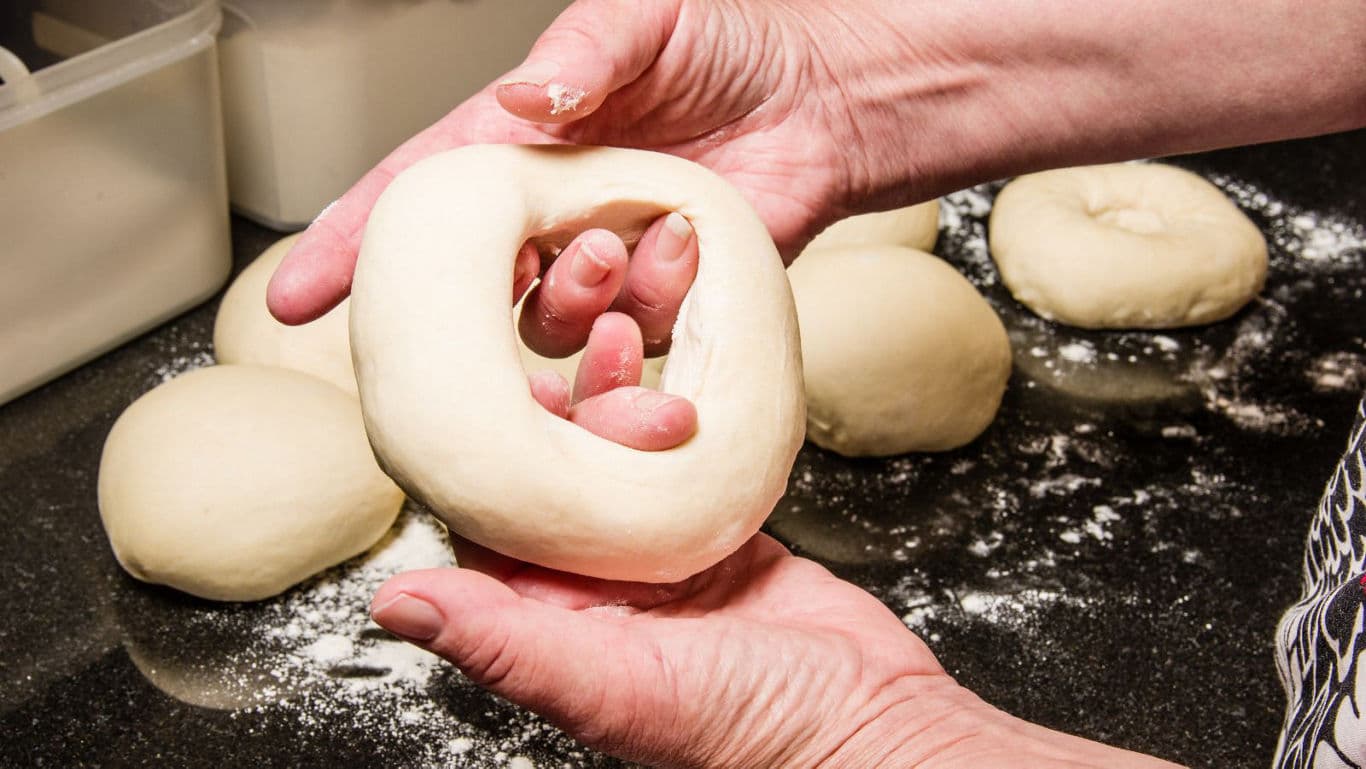 Hands shaping fresh bagel dough ring