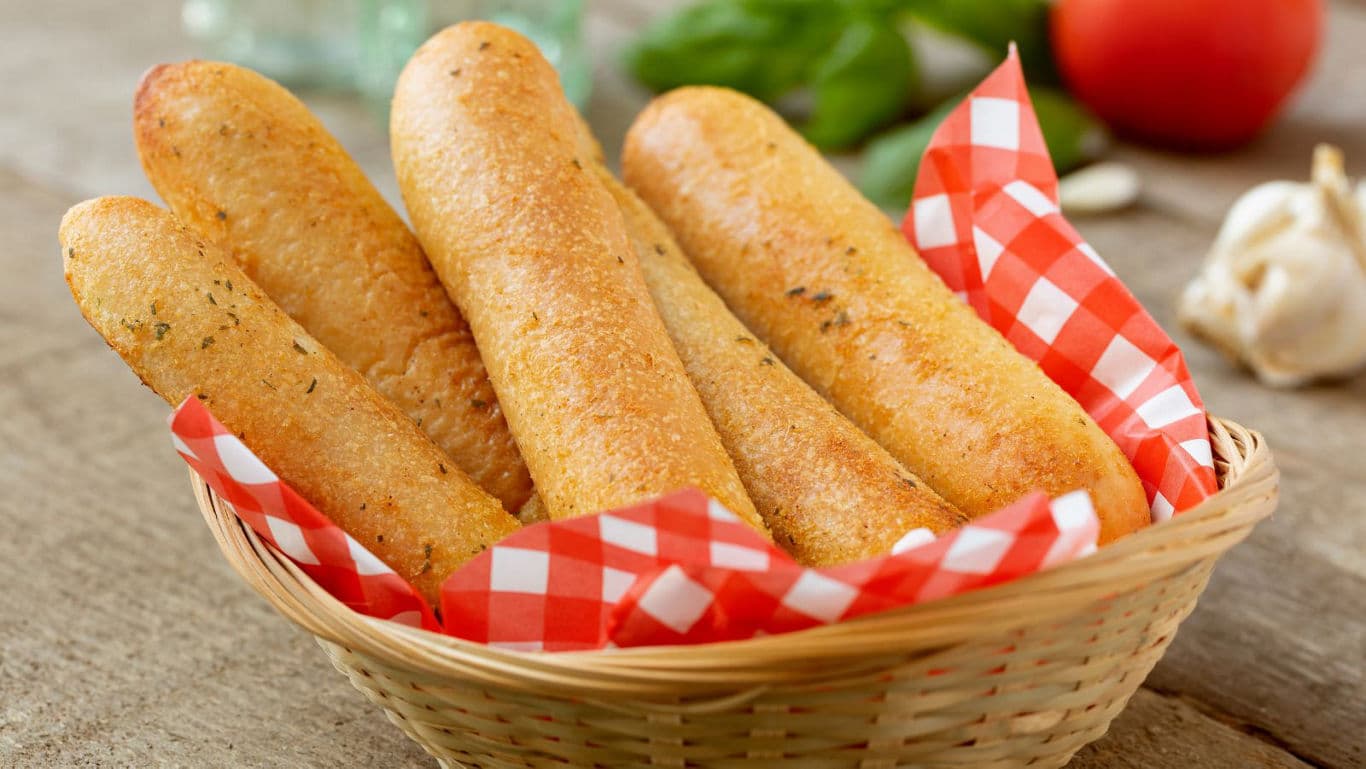 Basket of golden garlic breadsticks on table