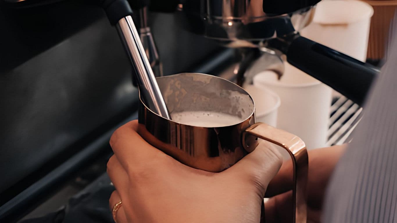 Barista steaming milk in metal pitcher