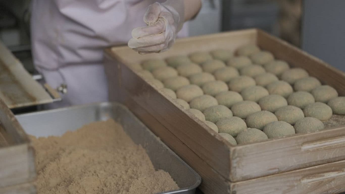 Person preparing traditional green mochi in bakery setting