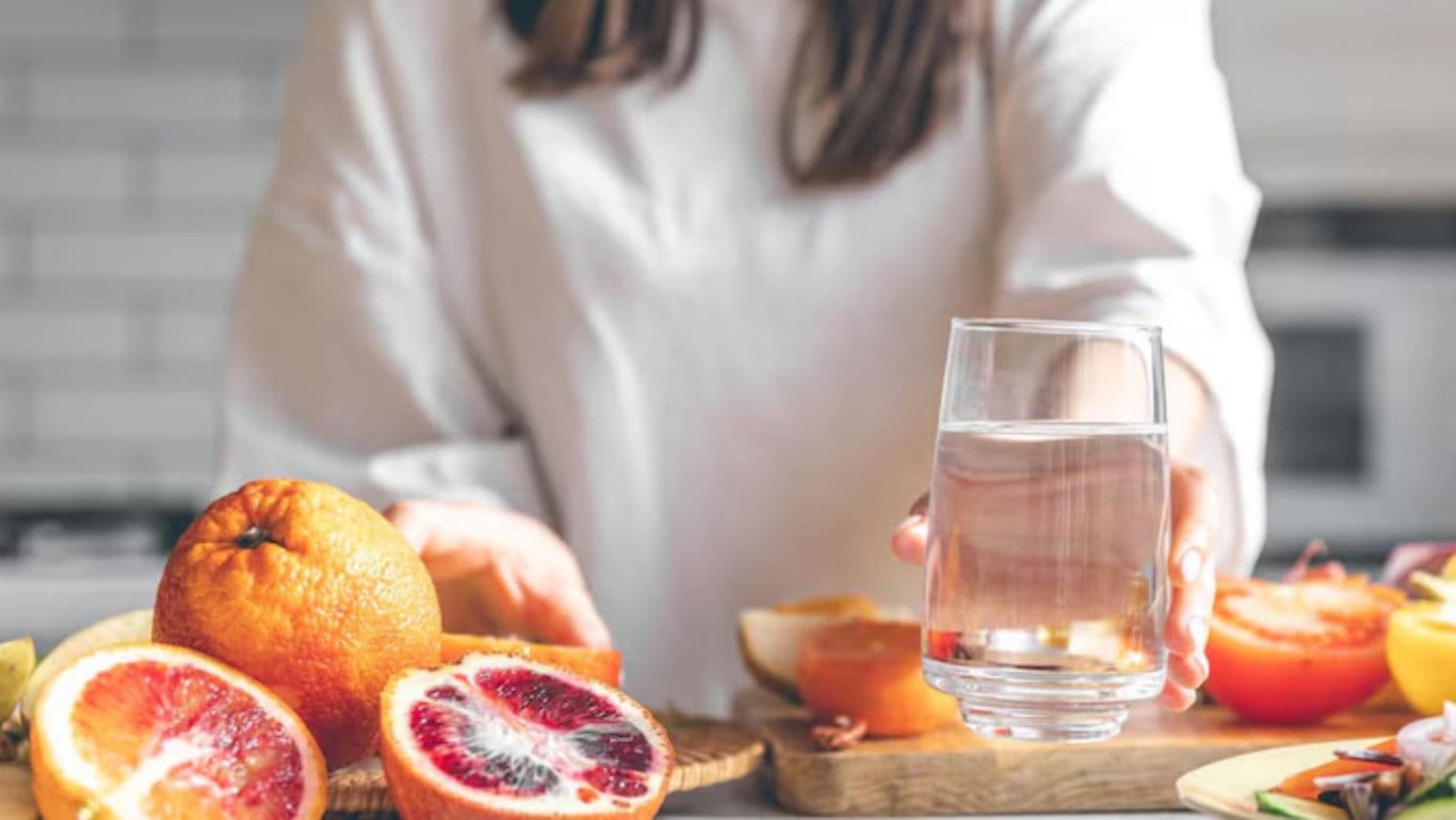 Woman holding glass of water near sliced citrus fruits