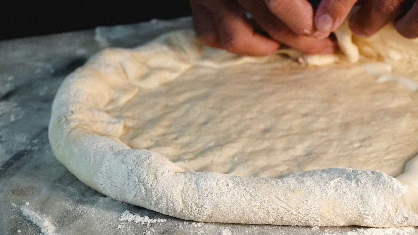 Chef shaping pizza dough crust by hand