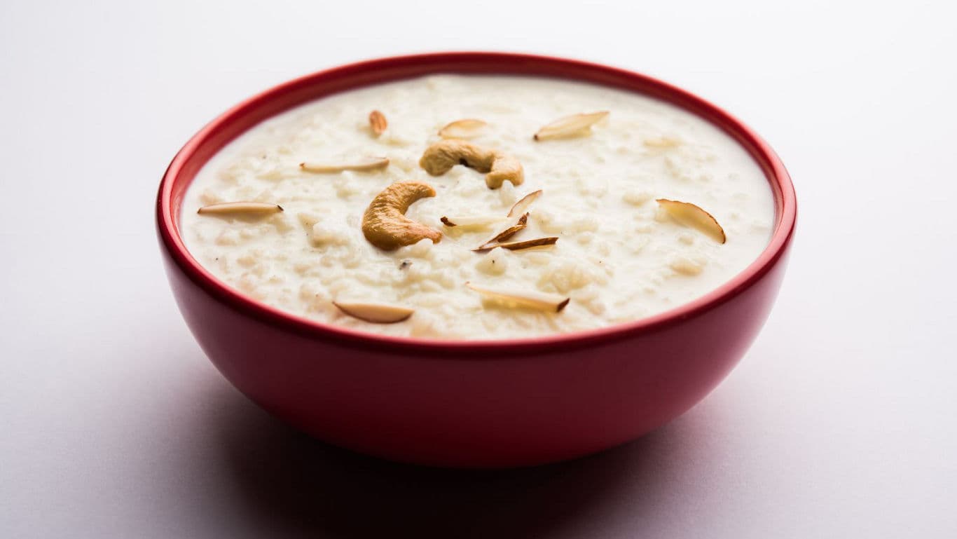 Creamy rice pudding garnished with nuts in red bowl
