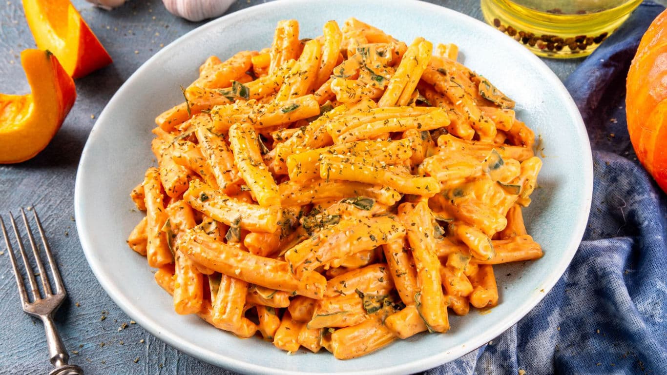 Creamy pumpkin pasta with herbs in white bowl