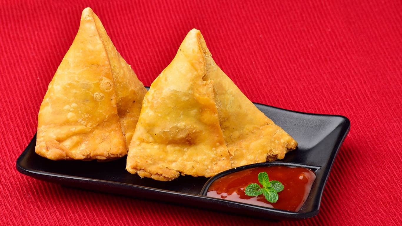 Crispy samosas with dipping sauce on black plate