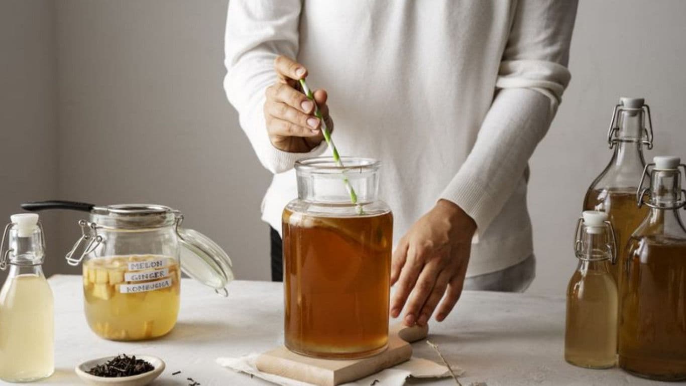 Person Preparing Kombucha with Glass Jars on Table