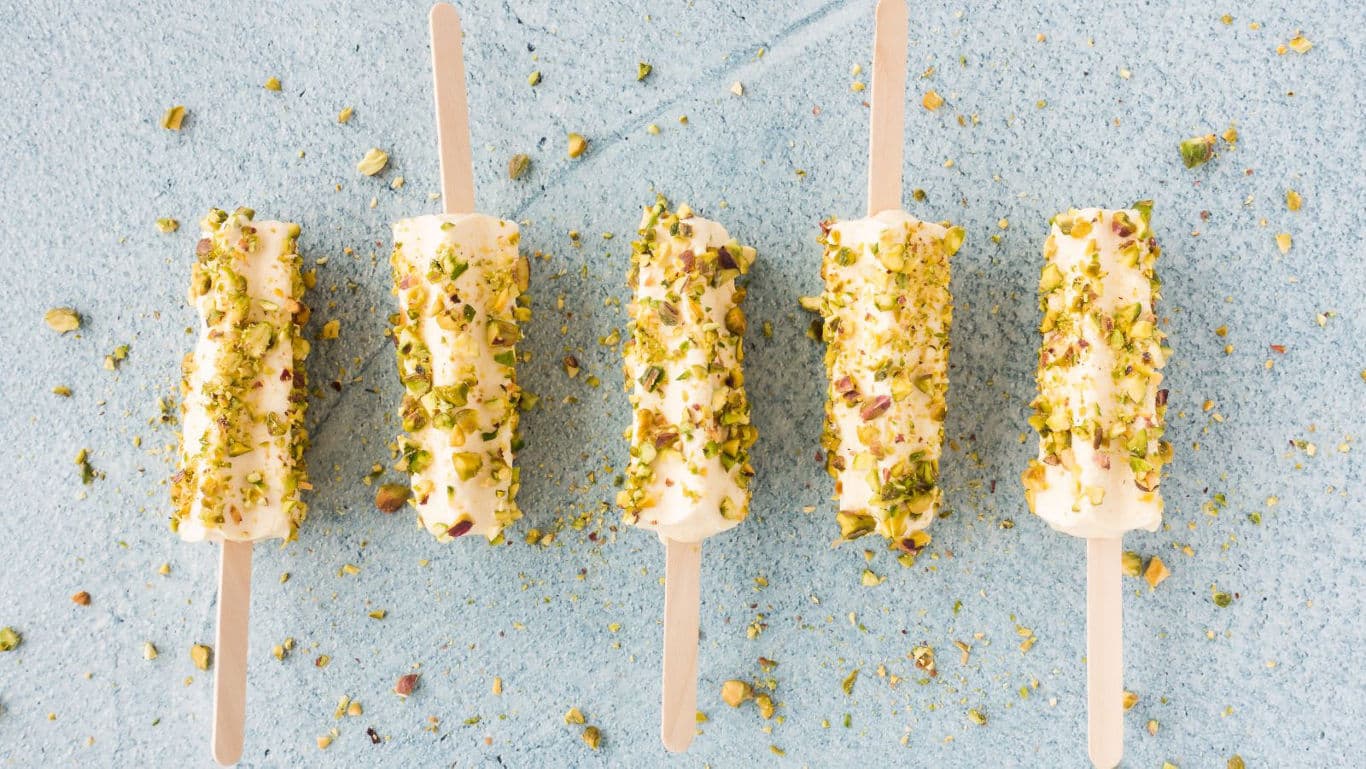 Pistachio coated ice cream popsicles on blue