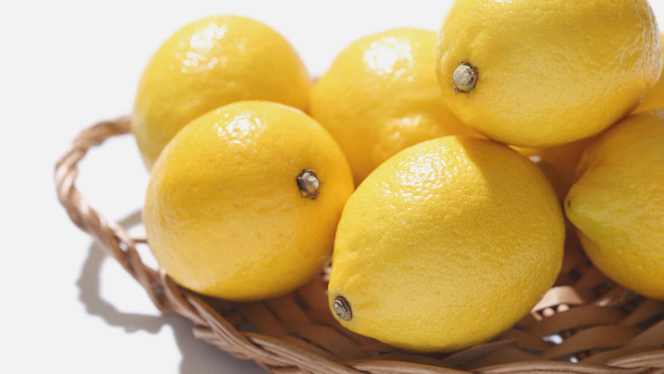 Fresh yellow lemons in wicker basket on white