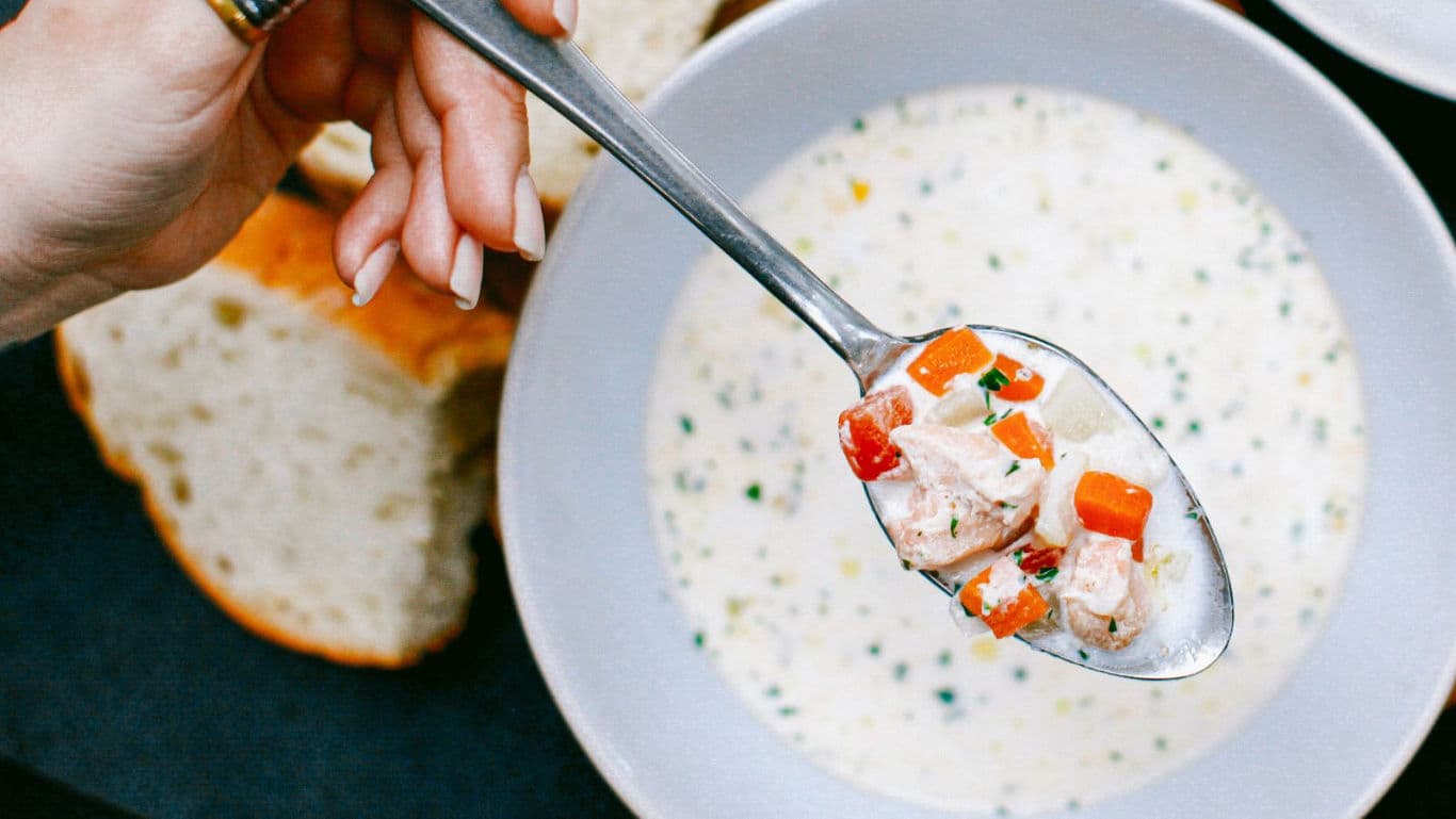 Hand holding spoonful of creamy soup