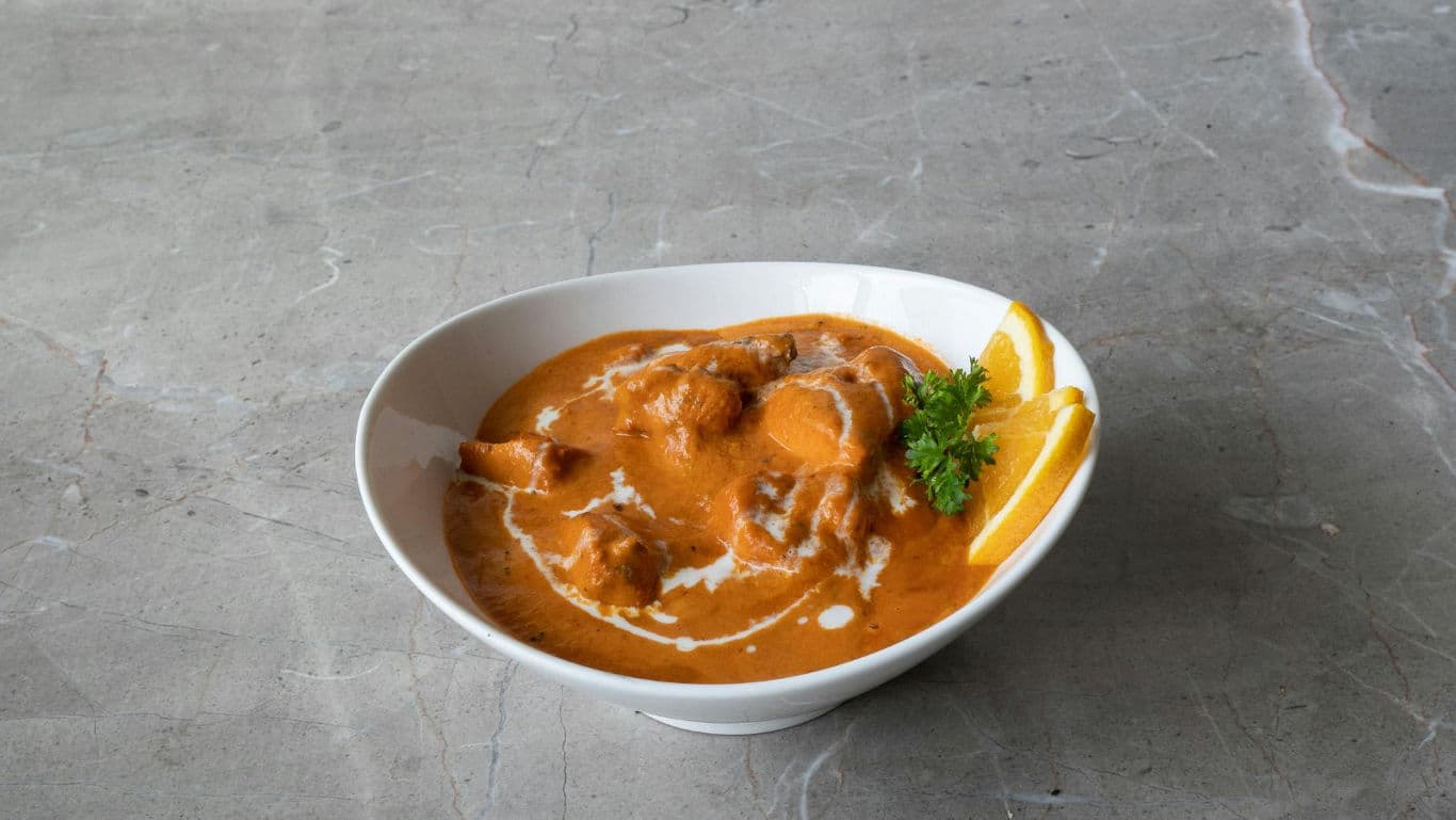 Bowl of creamy curry with garnish on stone