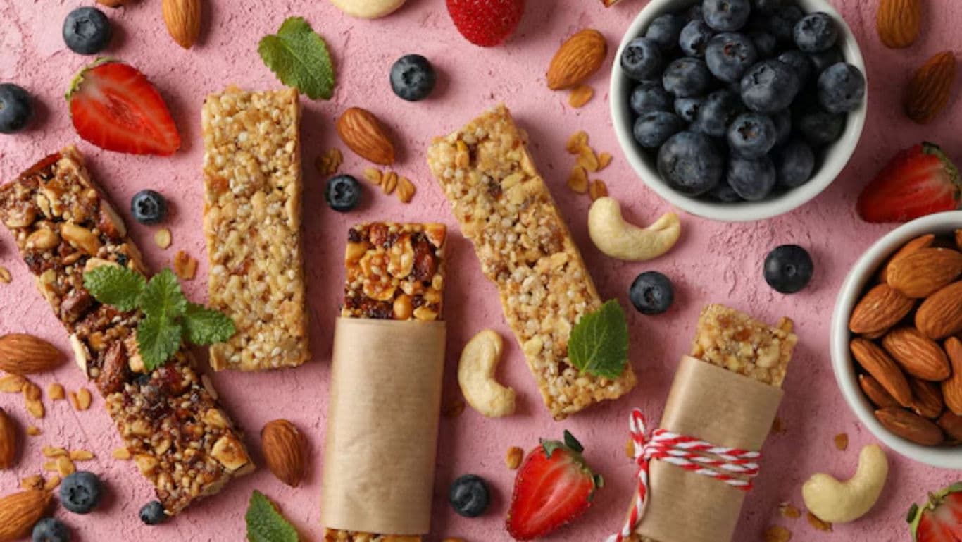 Assorted granola bars with berries and nuts on pink background