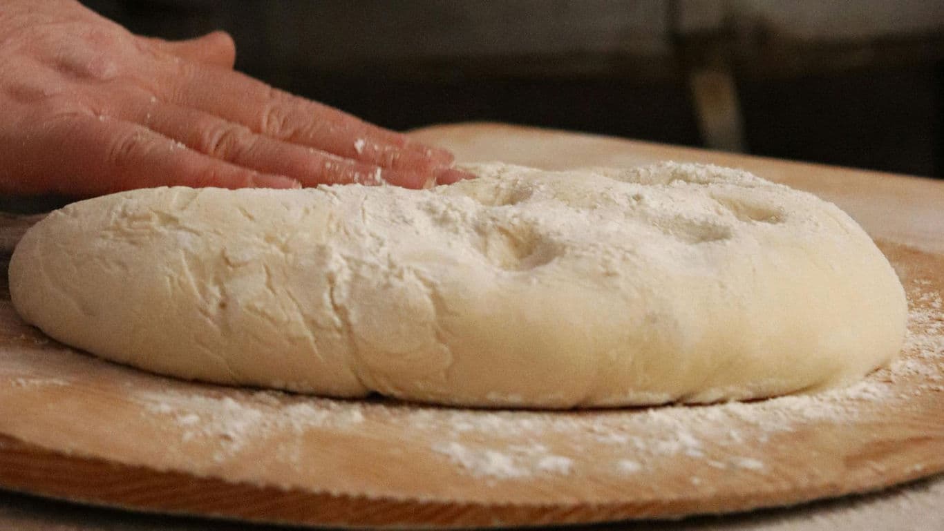 Hand shaping fresh bread dough on wooden board