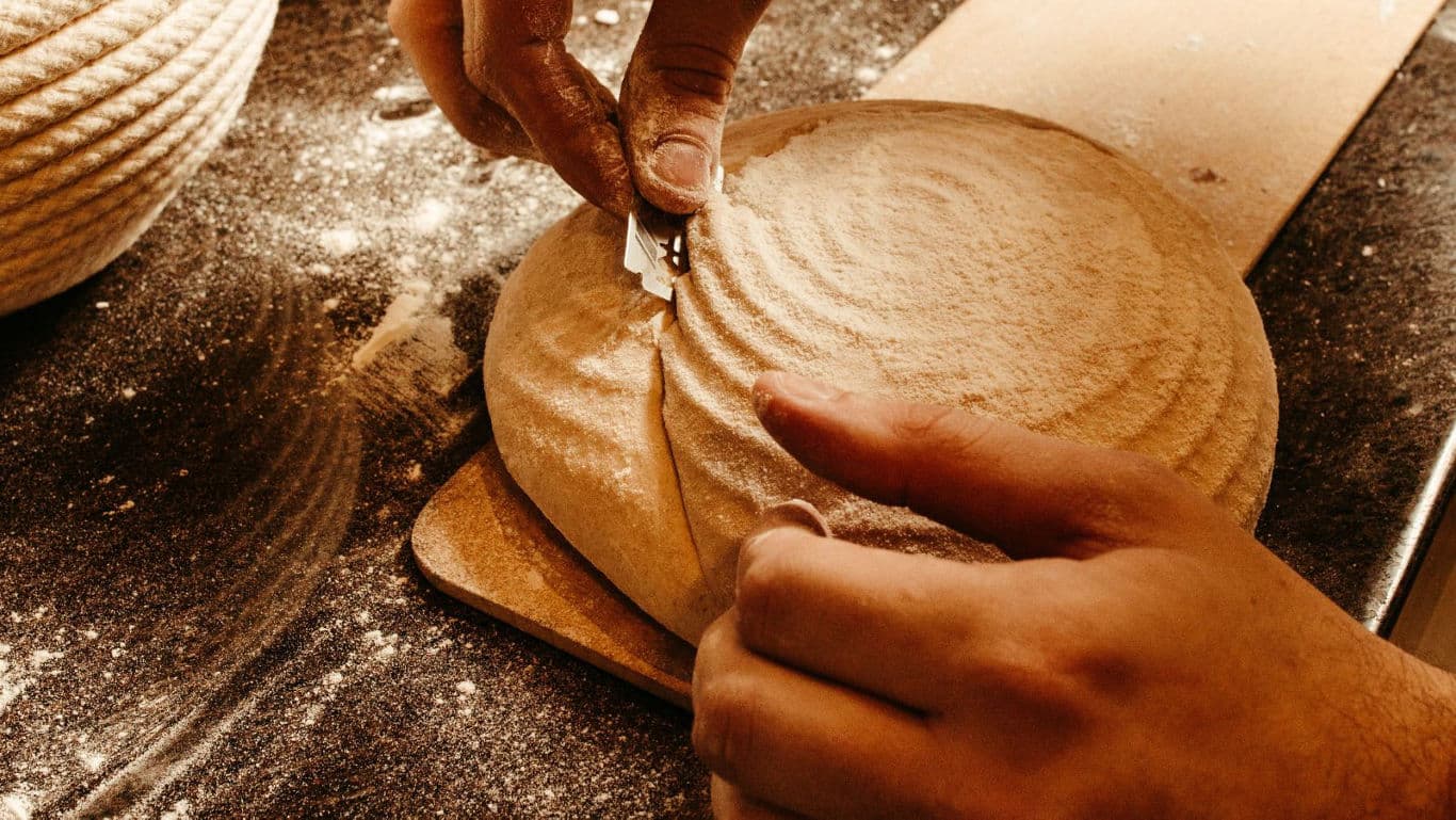 Baker scoring artisan bread dough by hand