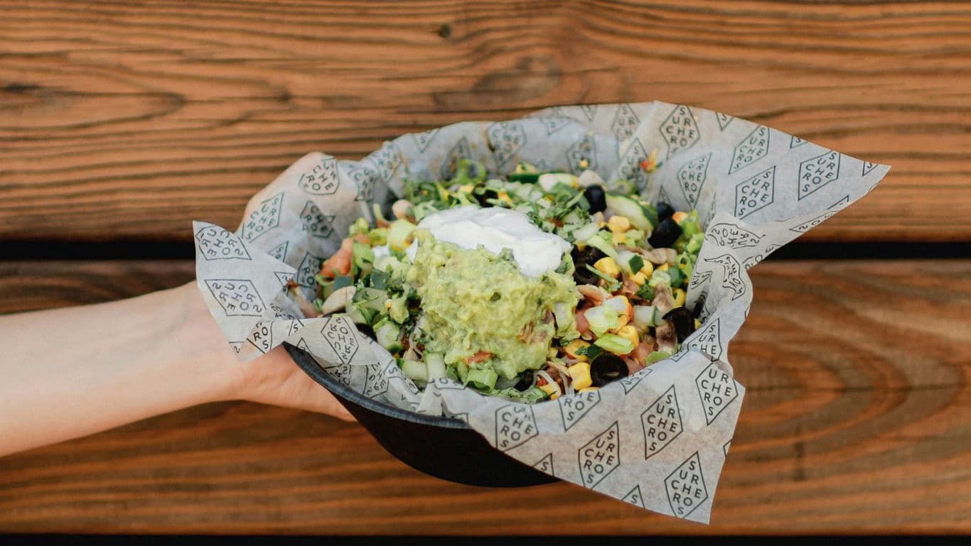 Hand holding fresh burrito bowl with guacamole topping