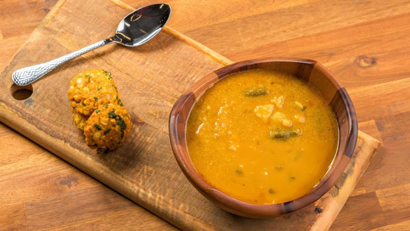 Wooden bowl of vegetable soup with fritter on board