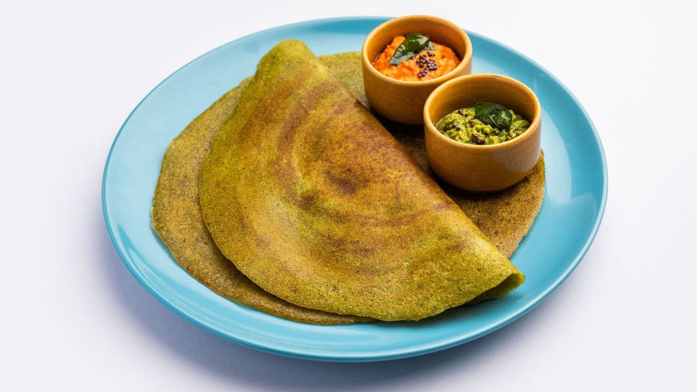 Green lentil dosa with chutneys on plate
