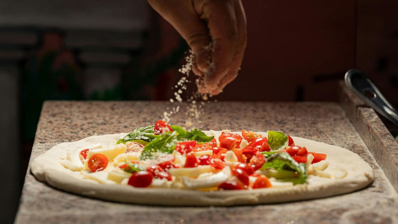 Chef sprinkling cheese over fresh pizza