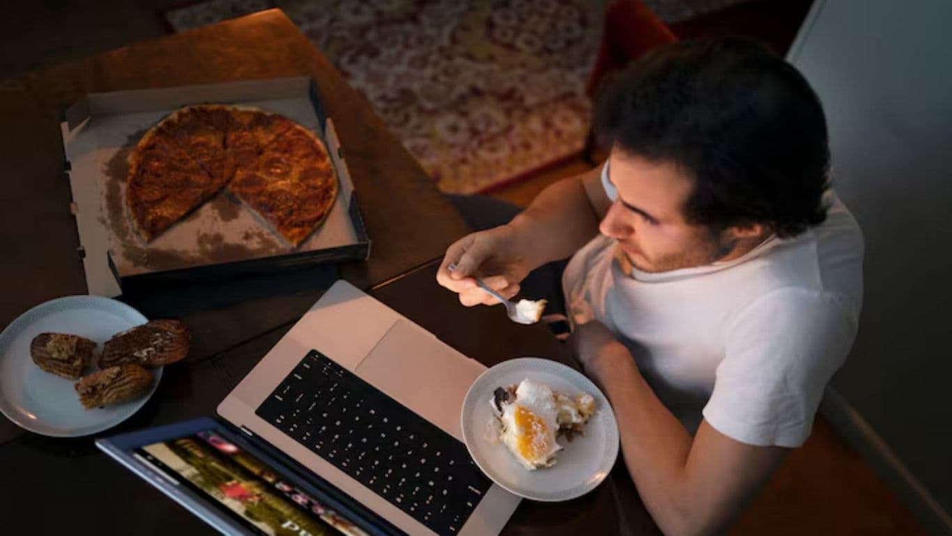 Person eating pizza and dessert while watching laptop