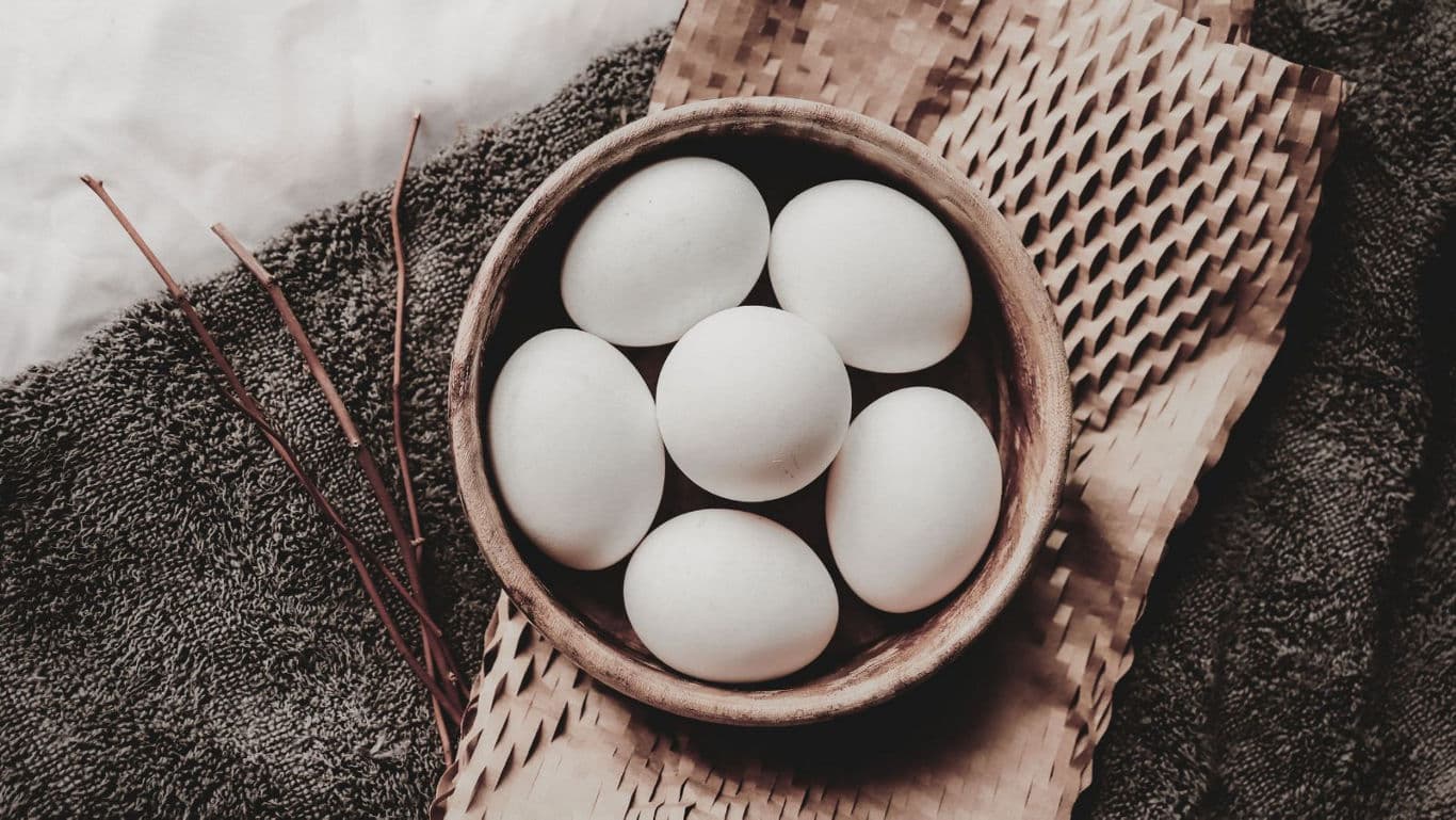 Rustic bowl of white eggs on textiles