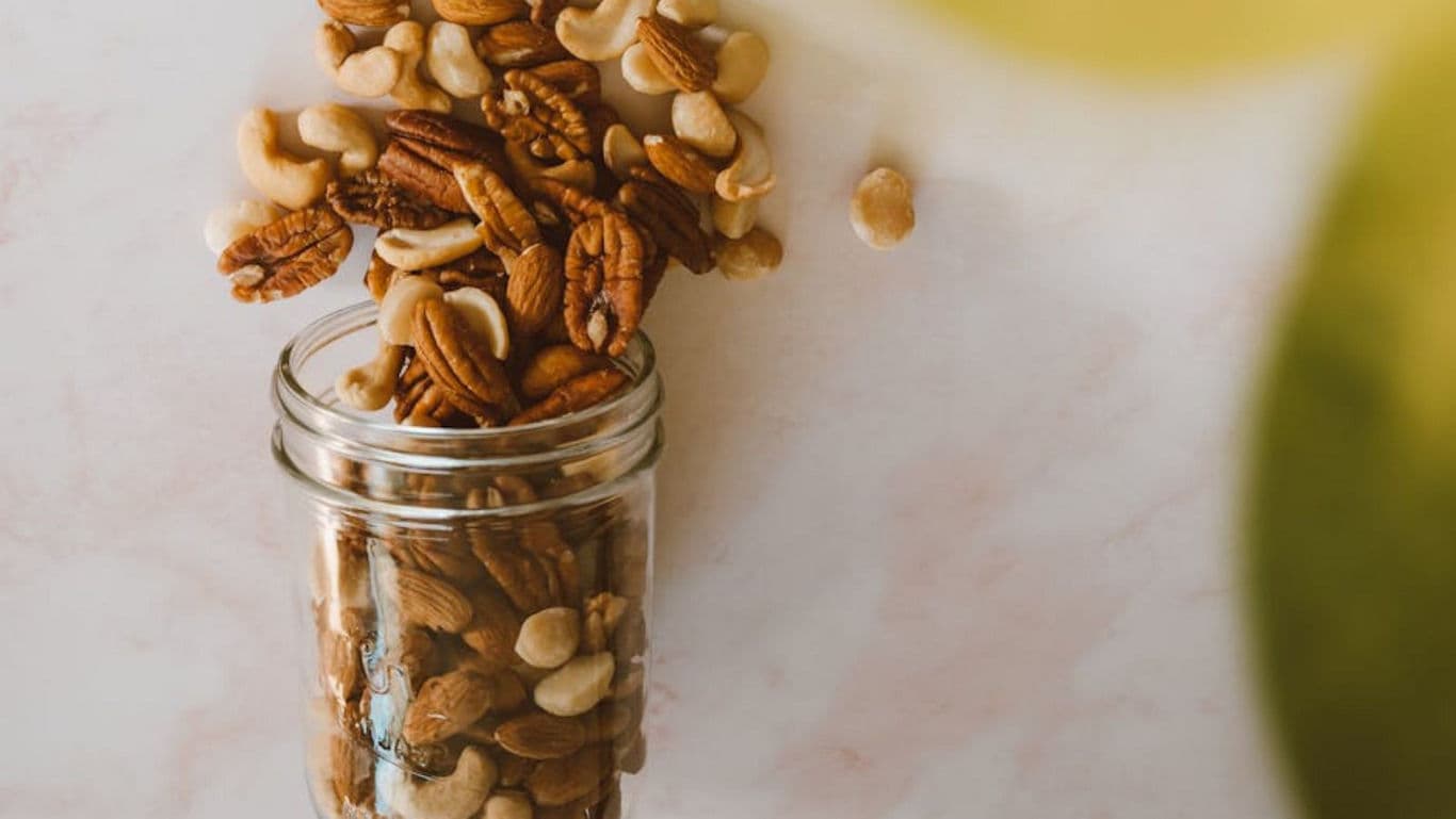 Mixed nuts spilling from glass jar on table