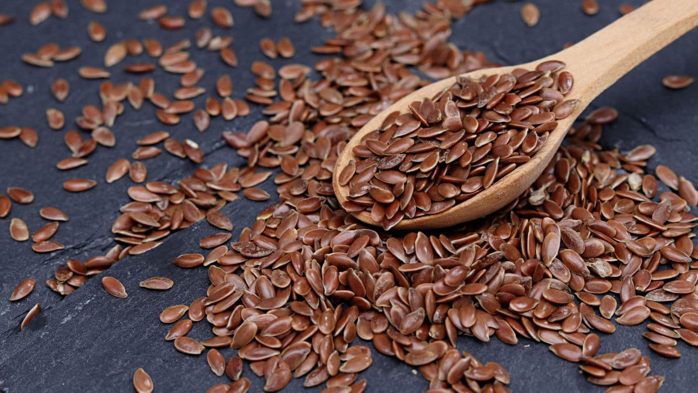 Brown flax seeds on slate with wooden spoon