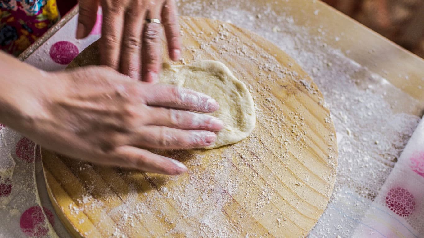 Hands shaping dough on floured wooden board