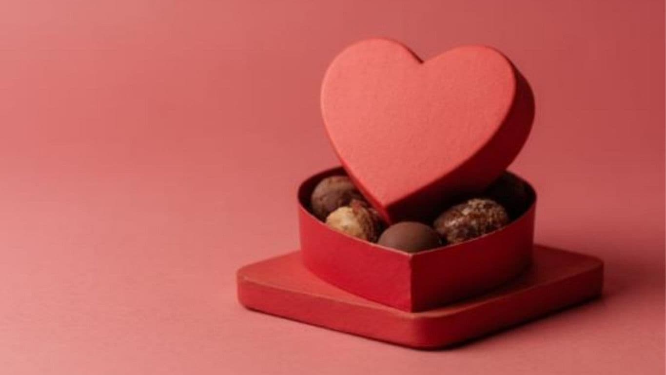 Heart-shaped chocolate box on pink background