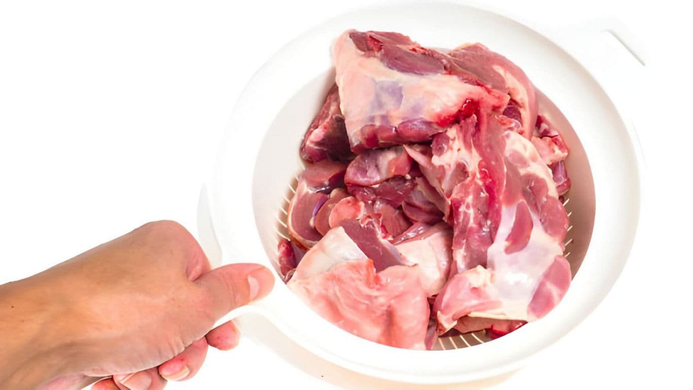 Raw meat pieces in white plastic strainer