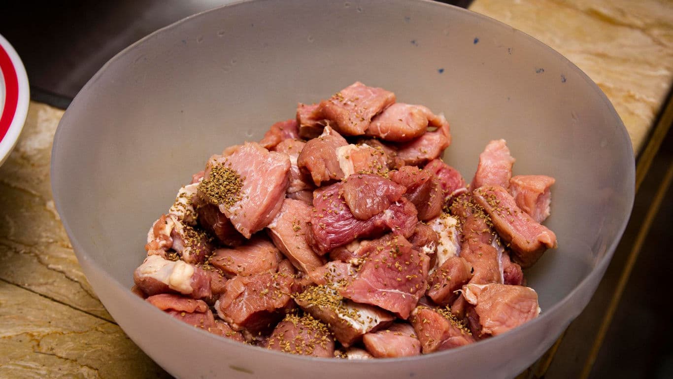 Seasoned raw meat cubes in mixing bowl