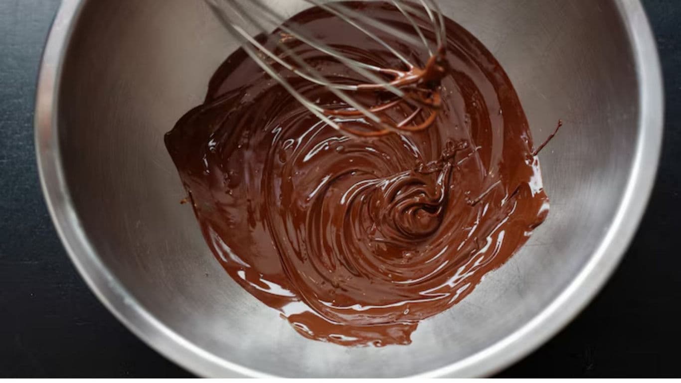 Whisk mixing melted chocolate in metal bowl