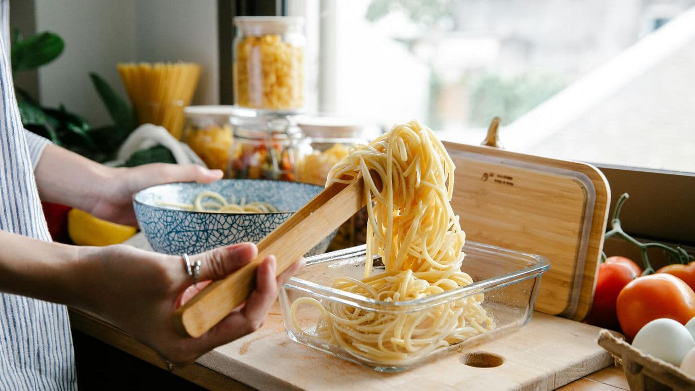 Person serving spaghetti into glass container