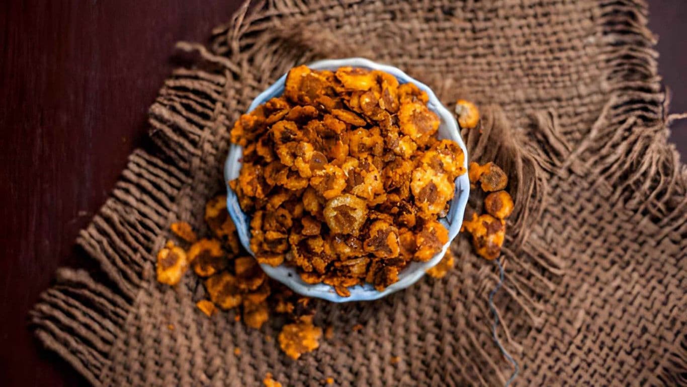 Spicy fried banana chips in ceramic bowl on burlap