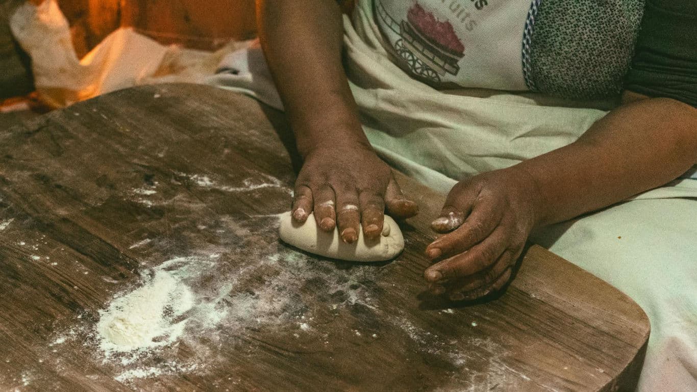 Person Kneading Dough on Wooden Surface Indoors