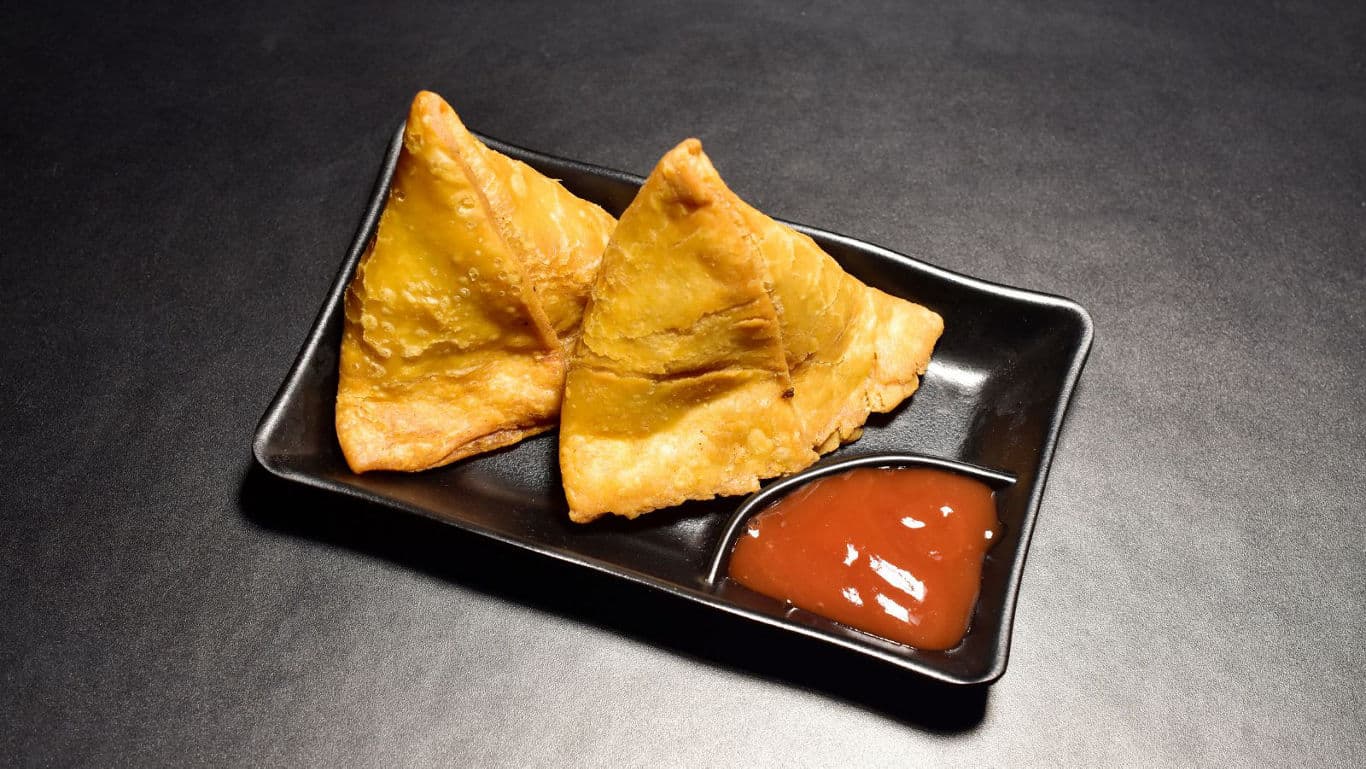 Two crispy samosas served with red chutney