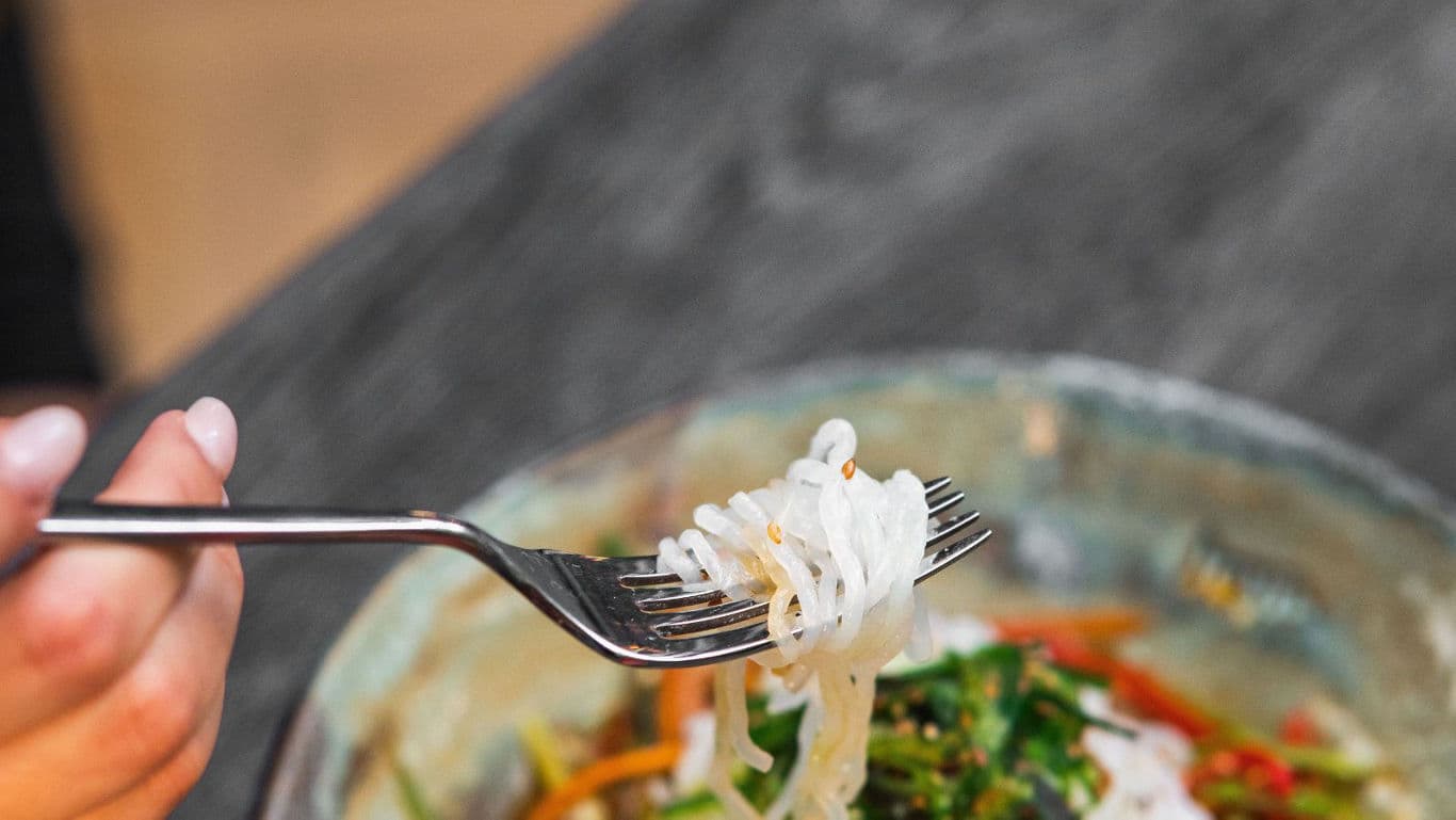 Fork lifting noodles from colorful salad bowl