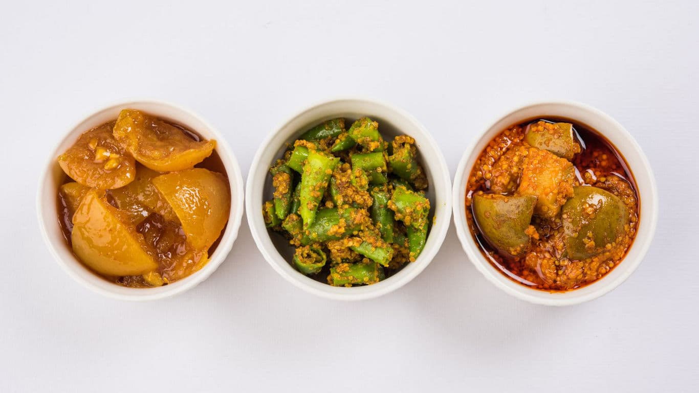 Three Indian pickles in white bowls on table