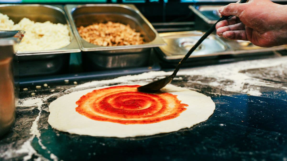 Spreading red tomato sauce on a pizza base. 