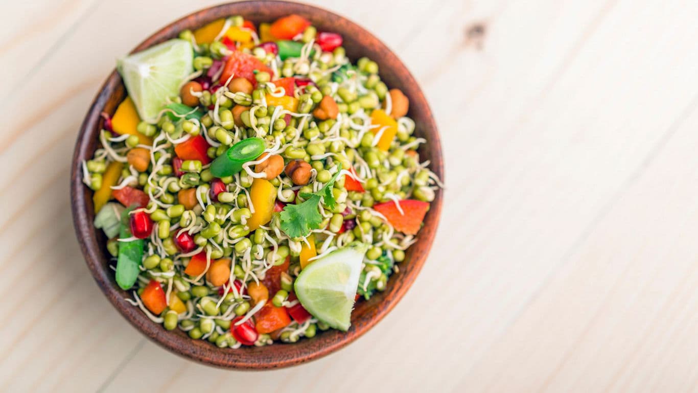Colorful sprouted salad with lime wedges in bowl