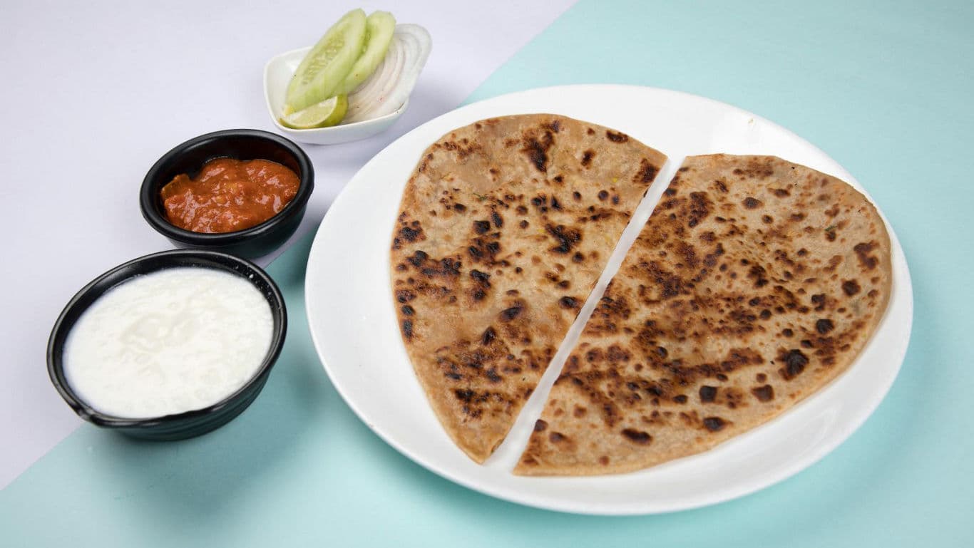 Stuffed paratha served with yogurt and chutney bowls
