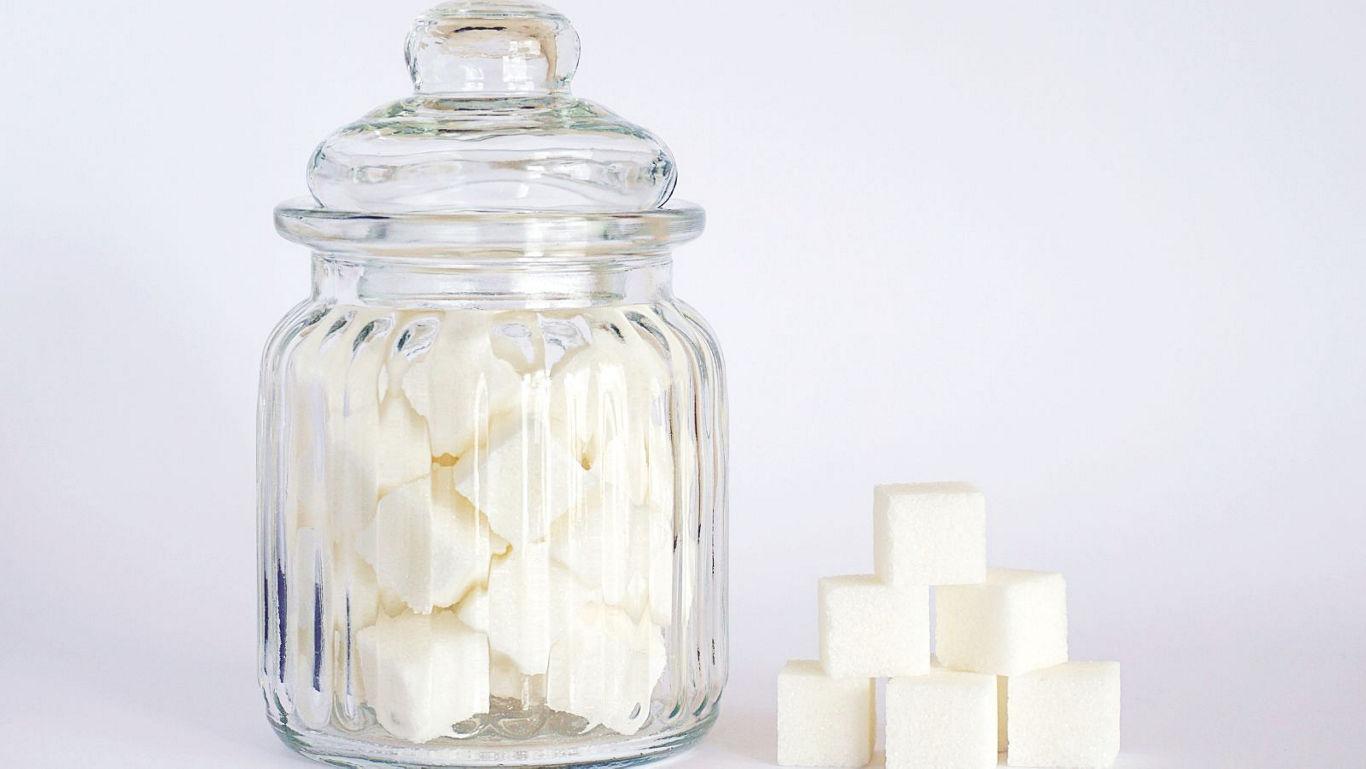 Glass jar with sugar cubes on white