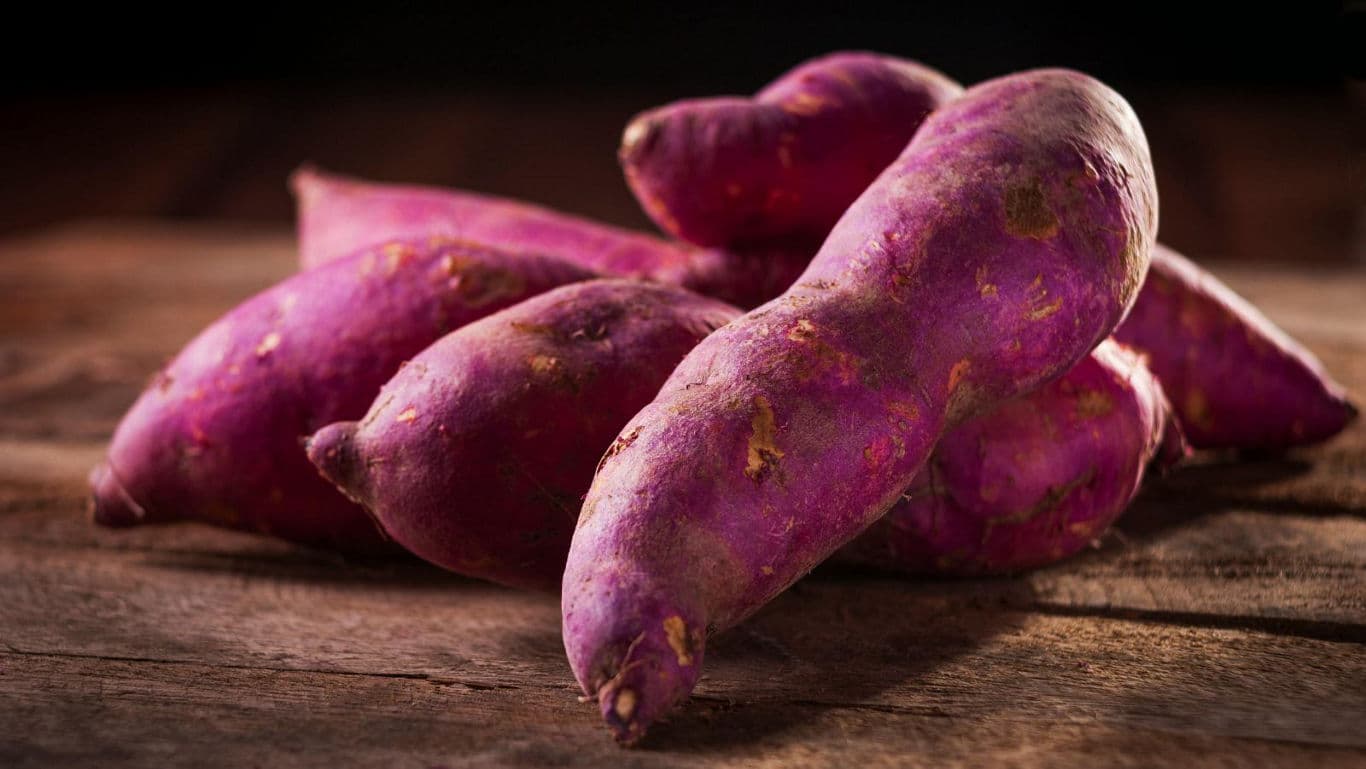 Fresh purple sweet potatoes on wooden surface