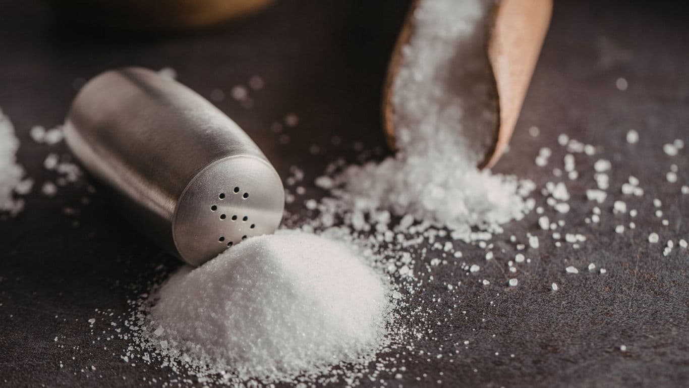 Salt spilled from shaker and wooden scoop