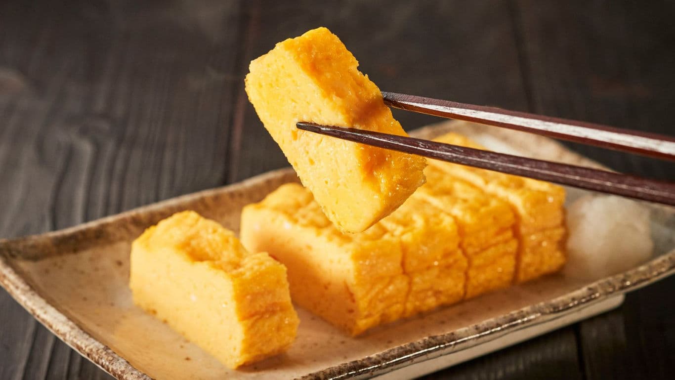 Chopsticks holding sliced Japanese tamagoyaki omelette